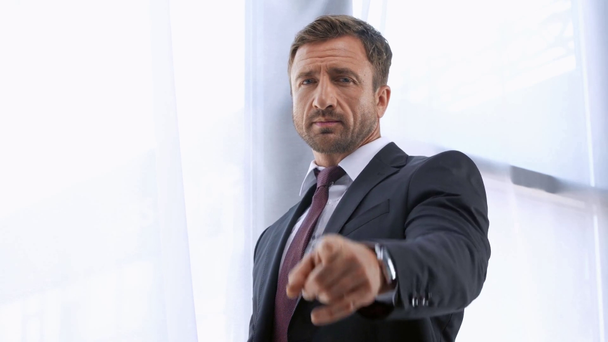 mature businessman pointing with finger at camera near window - Felvétel, videó