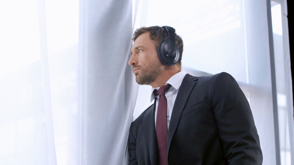 Reifer Geschäftsmann hört Musik über Kopfhörer am Fenster - Filmmaterial, Video