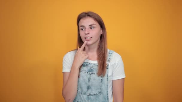 Fiatal nő visel fehér póló, több mint narancssárga háttér mutatja érzelmek - Felvétel, videó