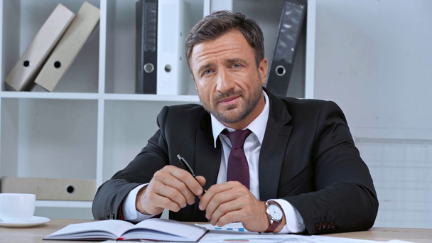 smiling mature businessman smiling while sitting at desk - Footage, Video