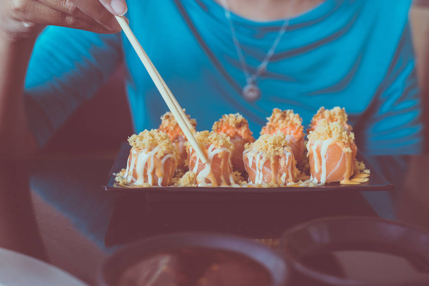 Kädet käyttäen syömäpuikkoja sushi rullina juustoa lautasen ja shoyu japani kastike ravintolassa
 - Valokuva, kuva