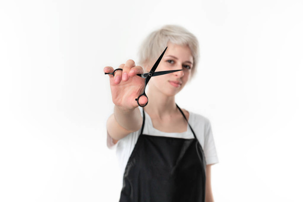 Pretty young hairdresser in white tee and black apron holding black scissors close to face ready for work standing isolated over white background. - Photo, Image