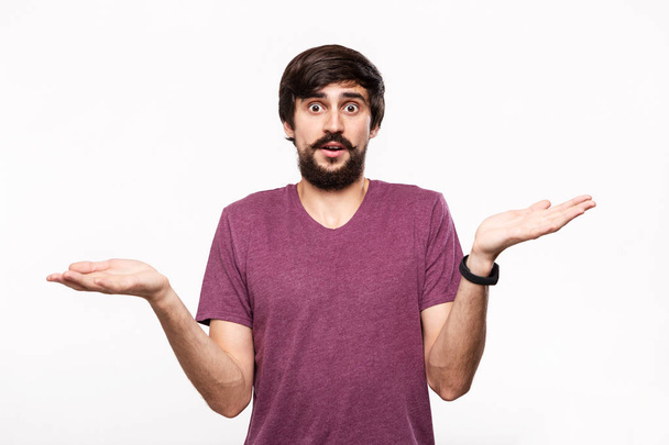 Excited brunet man in a yellow shirt with beard and mostaches shrugging his shoulders being surprised standing isolated over white background. - Foto, afbeelding