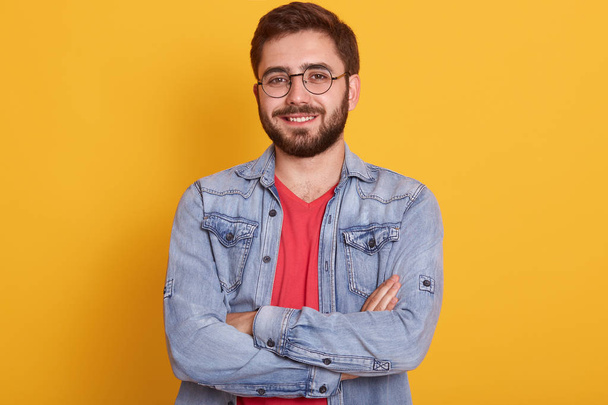 Close up portrait of bearded man with folded hands, sytanding and looking directly at camera with happy facial expression, being in good mood, handsome male dressed stylish clothing. People concept. - Foto, imagen