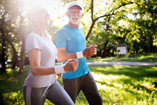 Beautiful senior couple running outside in sunny forest - Photo, Image