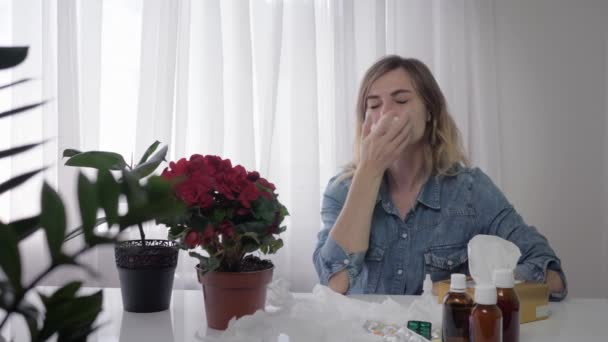 seizoensgebonden griep, jonge mooie vrouw lijdt een allergische reactie en voortdurend niezen en veegt haar neus met servet terwijl zittend aan tafel met medicijnen - Video