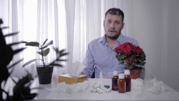 seizoensgebonden griep, jonge zieke man lijdt aan symptomen van ziekte niest en blaast zijn neus in zakdoek terwijl zittend aan tafel met medische geneesmiddelen - Video