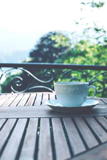 White ceramic cup of tea on a saucer on wooden table against picturesque background. - Photo, Image