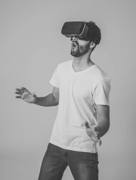 Casual bearded young man using VR headset glasses goggles feeling excited trying simulation, exploring virtual reality making gestures interacting with new 3D world. In new technology concept. - 写真・画像