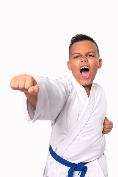 Karate young boy in white uniform makes a hit aggressively shouting, isolated - Photo, Image
