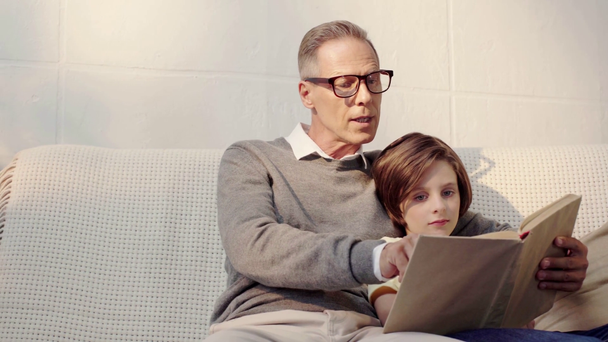 Dziadek i wnuk czytając książkę razem w salonie - Materiał filmowy, wideo