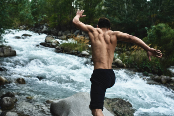 Kazakh muscular athlete man trains and exercises by the river in nature. Asian handsome does extreme fitness workout outdoors - Fotoğraf, Görsel