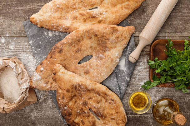 top view of lavash bread on gray towel near rolling pin, package with flour, fresh parsley and olive oil on wooden table - Photo, Image