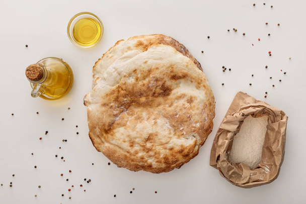 Widok z góry Lavash chleb w pobliżu mąki i oliwy z oliwek na białej powierzchni z pieprzu - Zdjęcie, obraz