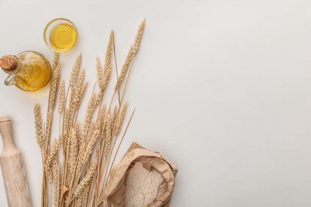 vista superior de espigas de trigo, rodillo, aceite de oliva y paquete de harina en la superficie blanca
 - Foto, Imagen