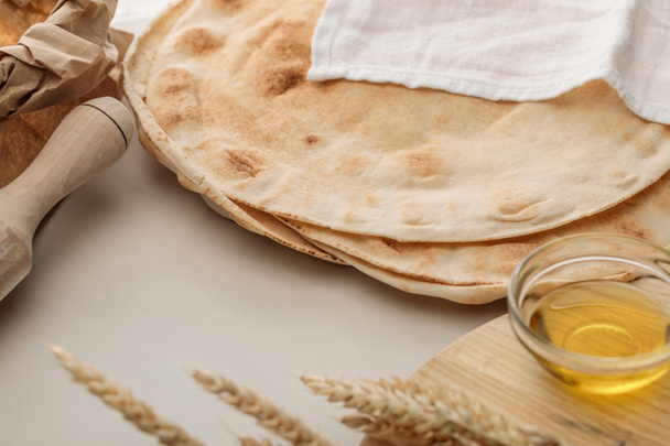 flat lavash bread covered with white towel near rolling pin and cutting board with spikes and oil - Photo, Image