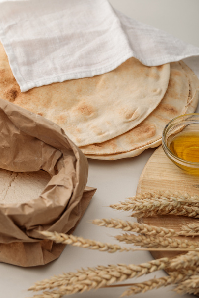 lavash bread covered with white towel near flour package and cutting board with spikes and oil - Foto, imagen