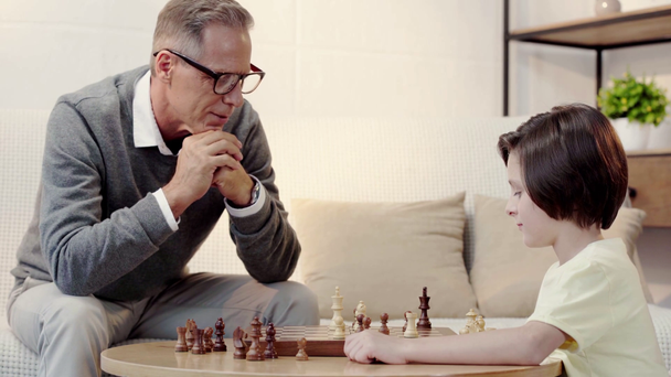 uśmiechnięty dziadek i wnuk grając w szachy w salonie - Materiał filmowy, wideo
