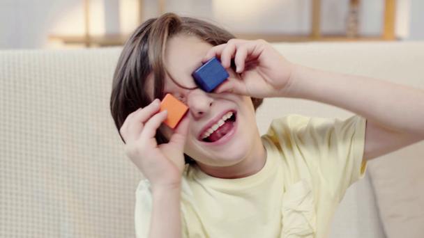 boy putting wooden cubes on eyes and showing tongue - Footage, Video