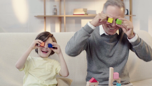 grandfather and grandson laughing while putting building blocks on eyes - Imágenes, Vídeo