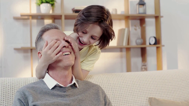 Enkel bedeckt Augen des glücklichen Großvaters mit Händen im Wohnzimmer - Filmmaterial, Video