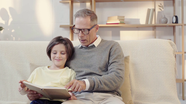 Opa und Enkel lesen gemeinsam Buch im Wohnzimmer - Filmmaterial, Video