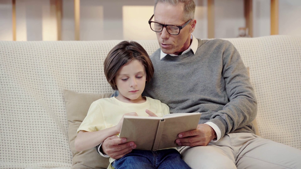 dědeček a vnuk čtení knihy společně v obývacím pokoji - Záběry, video