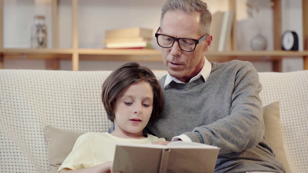 dziadek i wnuk czytają razem książkę w salonie - Materiał filmowy, wideo