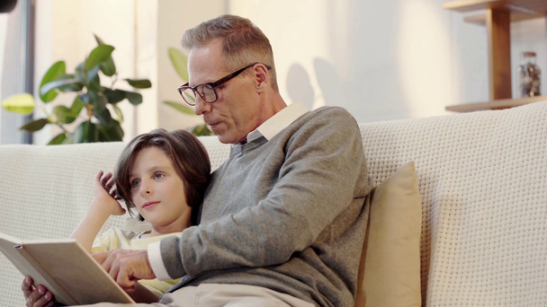 grandpa and grandson reading book together in living room - Metraje, vídeo