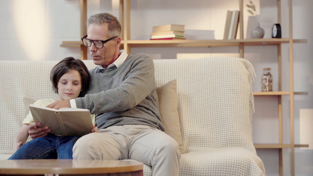 grandpa and grandson reading book together in living room - Filmagem, Vídeo