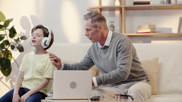 grandfather offering grandson to read book while boy listening music in headphones - Footage, Video