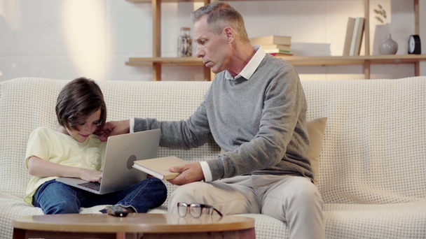 büyükbaba dizüstü bilgisayar kullanırken çocuk kitap okumak için torunu sunan - Video, Çekim