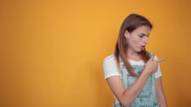 Νέα γυναίκα φορώντας λευκό μπλουζάκι, πάνω από πορτοκαλί φόντο δείχνει τα συναισθήματα - Πλάνα, βίντεο