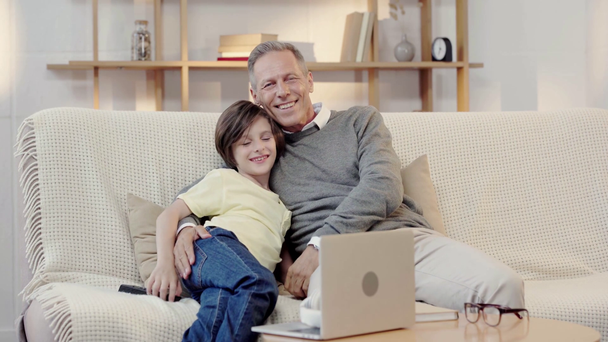 happy grandfather and grandson hugging and watching TV together in living room - Footage, Video