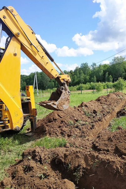 Una excavadora amarilla cavando una zanja en el sitio de construcción, un primer plano, contra el cielo
. - Foto, imagen