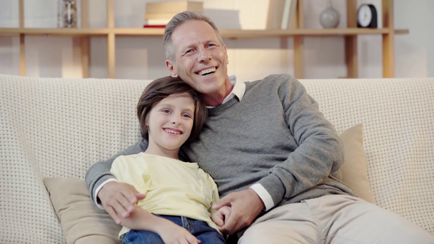 happy grandfather and grandson embracing and watching TV together in living room - Filmagem, Vídeo