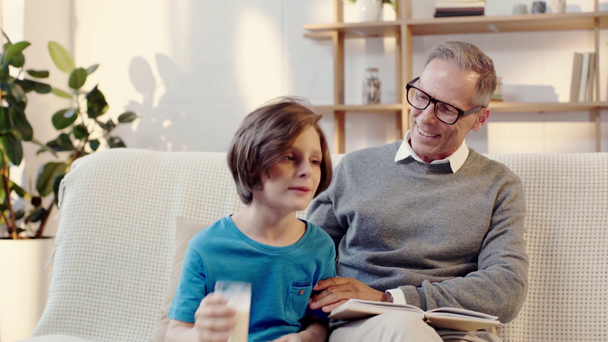 dědeček čtení knihy, objímání s vnukem, který pije mléko - Záběry, video