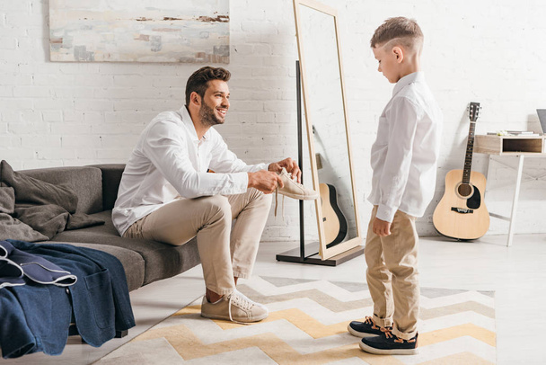 son looking at father while he tying shoelaces at home - Fotoğraf, Görsel