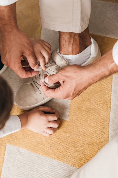 cropped view of father teaching son to tying shoelaces at home - Фото, зображення