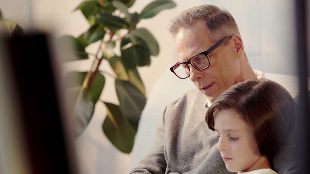 selective focus of grandfather in glasses and grandson reading book - Materiał filmowy, wideo