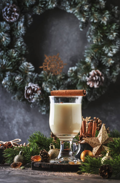 New Year or Christmas Eggnog cocktail - hot winter or autumn drink with milk, eggs and dark rum, sprinkled with cinnamon and nutmeg in a glass on wooden background, festive decoration - Foto, immagini
