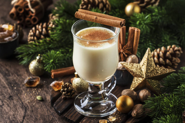 New Year or Christmas Eggnog cocktail - hot winter or autumn drink with milk, eggs and dark rum, sprinkled with cinnamon and nutmeg in a glass on wooden background, festive decoration - Фото, зображення