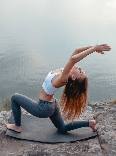 The girl practices yoga. Surrounded by nature on the island's mountain and riverbank. - Valokuva, kuva