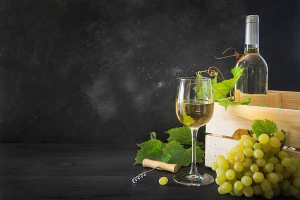 Bottle of white wine with wineglass, ripe grape on black wooden table. - Fotografie, Obrázek