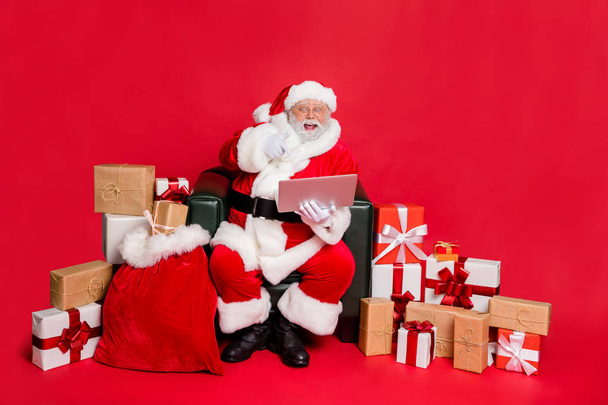 Nice cheerful excited glad hard-working fat bearded man delivering purchases shop delivery checking address list clients children orders isolated on bright vivid shine red background - Foto, afbeelding