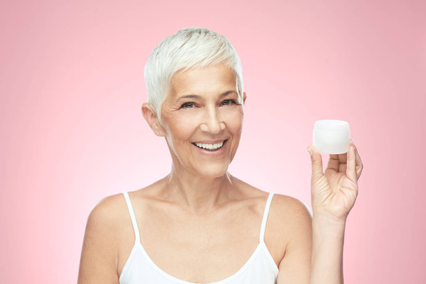 Gorgeous smiling Caucasian senior woman trying out new anti age cream and looking at camera. Beauty photography. - Foto, imagen