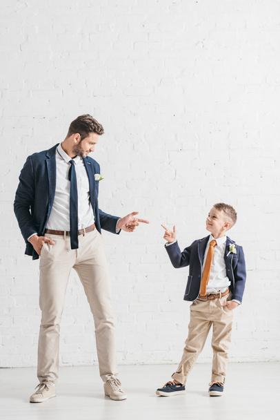 full length view of father and son in jackets with boutonnieres looking at each other - Foto, Imagen