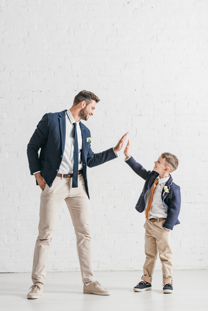 full length view of father and son in jackets with boutonnieres looking at each other - Фото, изображение