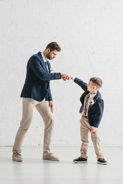 full length view of father and son in jackets with boutonnieres looking at each other - Foto, Imagem