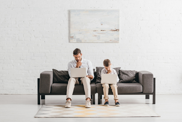 dad and son in formal wear using laptops while sitting on sofa - Φωτογραφία, εικόνα